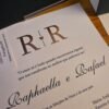 Convite de casamento luxuoso aberto, mostrando nomes dos noivos, acabamento em relevo e detalhes da cerimônia